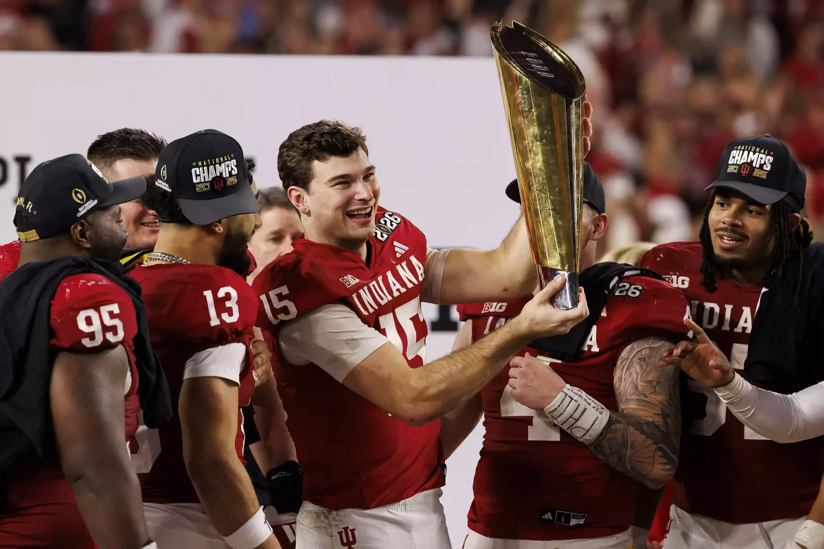 Fernando Mendoza holding the College Football Playoff National Championship trophy, surrounded by his teammates.
